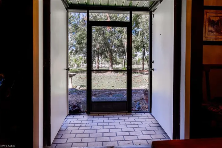 Screened Front Entryway Featuring Double Front Doors Overlooking Palm Tree Lined Driveway.