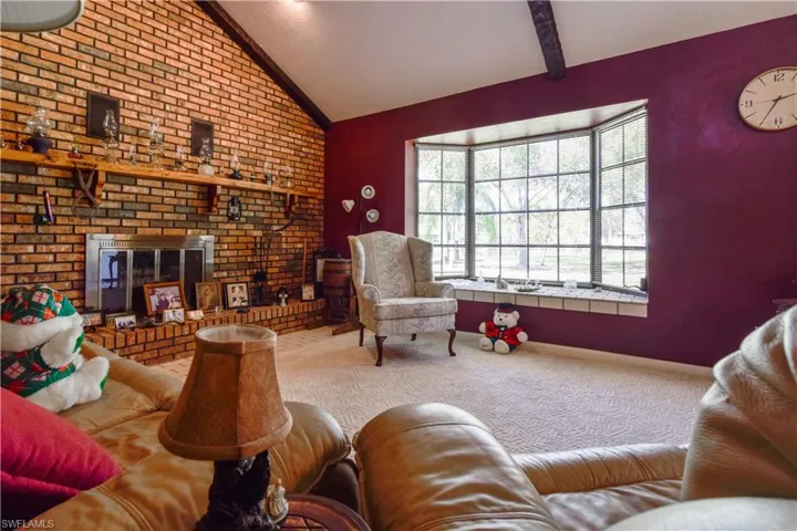 Great Room Area Featuring Soaring Ceilings A Bricked Wall With Woodburning Fireplace And Hearth, Wood Beams, And Window Seat In The Bay Window Overlooking The Private Lake.