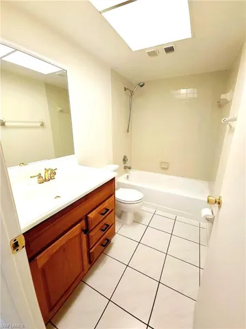 Bathroom featuring a wood-finish vanity with a white countertop, a white toilet, and a white tub with shower