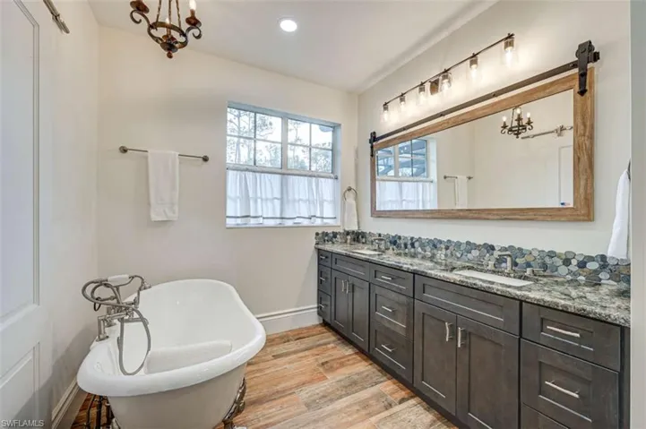 Bathroom featuring hardwood / wood-style floors, a tub to relax in, dual vanity, and an inviting chandelier