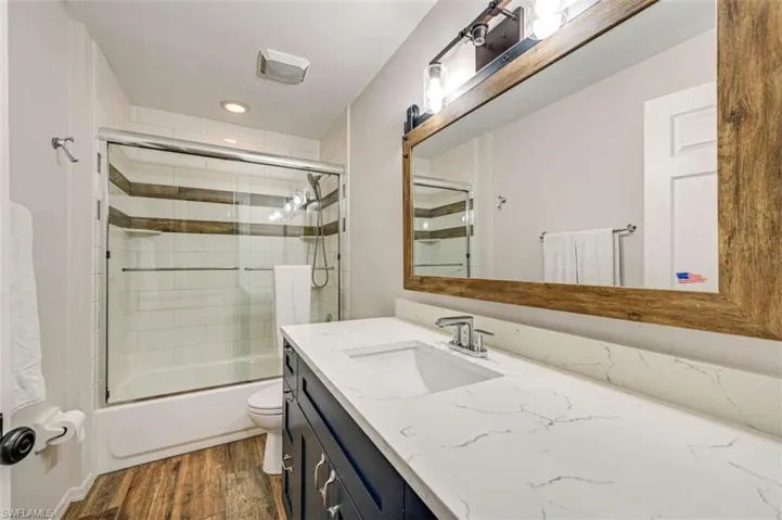 Full bathroom with hardwood / wood-style floors, shower / bath combination with glass door, vanity, and toilet