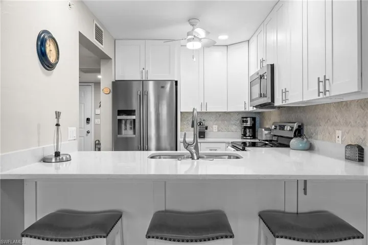 Beautiful breakfast bar area, stainless steel appliances, quartz countertops, white cabinetry, and lovely backsplash