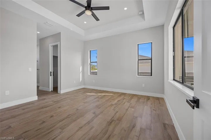 Unfurnished room with light wood-type flooring, plenty of natural light, ceiling fan, a raised ceiling, and recessed lighting