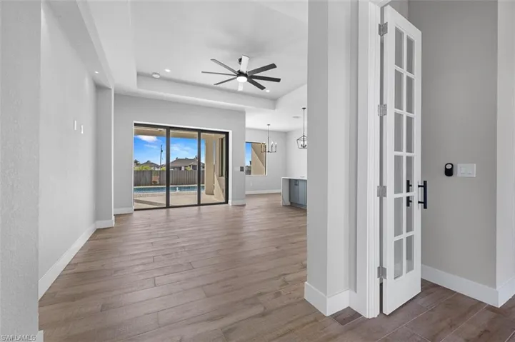 Unfurnished living room featuring a raised ceiling, wood finished floors, a ceiling fan, recessed lighting, and a chandelier