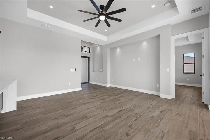 Unfurnished living room with a tray ceiling, ceiling fan, wood finished floors, recessed lighting, and a chandelier