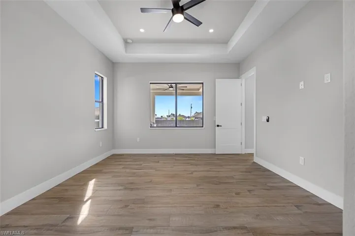 Empty room featuring ceiling fan, a tray ceiling, wood finished floors, and recessed lighting