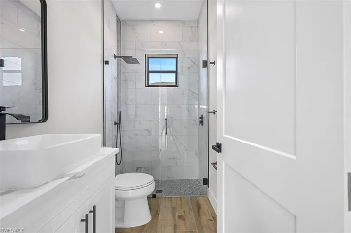 Full bath with vanity, a marble finish shower, wood finished floors, and recessed lighting