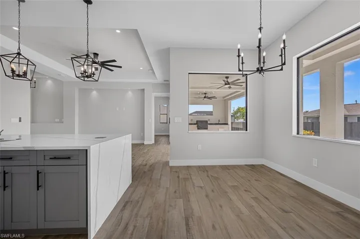 Unfurnished dining area featuring a chandelier, light wood-style flooring, a ceiling fan, recessed lighting, and a tray ceiling
