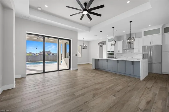 Kitchen featuring a tray ceiling, stainless steel appliances, a chandelier, recessed lighting, and wall chimney range hood