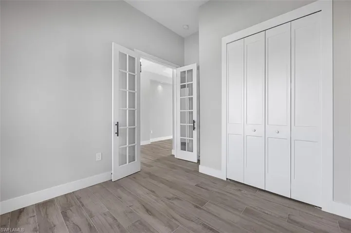 Unfurnished bedroom featuring french doors, wood finished floors, a closet, and vaulted ceiling
