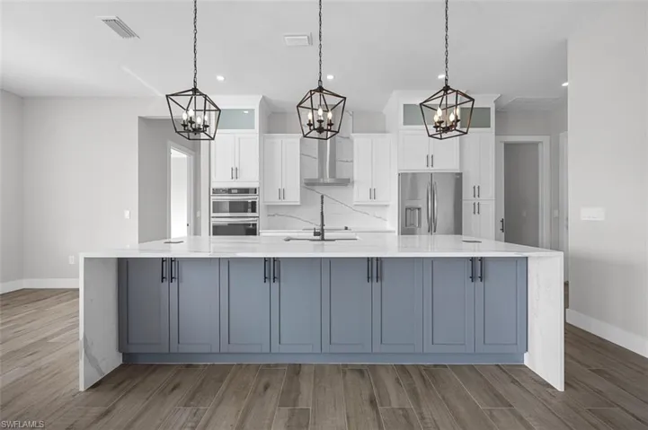 Kitchen featuring a chandelier, a large island with sink, white cabinetry, wood finished floors, and recessed lighting