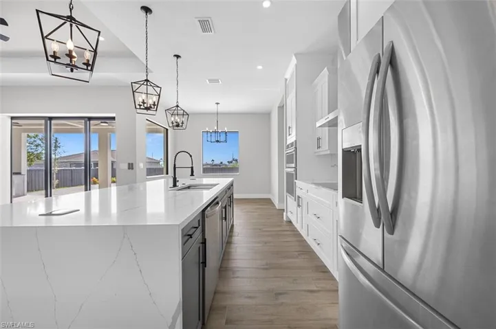Kitchen with appliances with stainless steel finishes, a chandelier, a large island with sink, recessed lighting, and white cabinetry