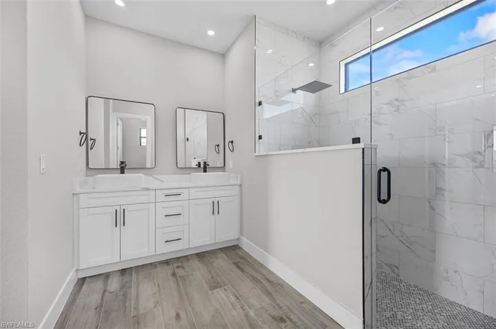 Bathroom featuring a marble finish shower, double vanity, wood finished floors, and recessed lighting