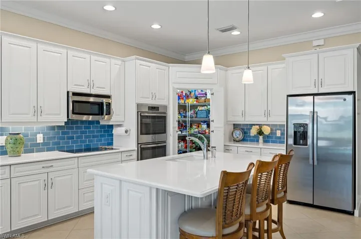 Kitchen featuring ornamental molding, white cabinets, an island with sink, decorative light fixtures, and stainless steel appliances