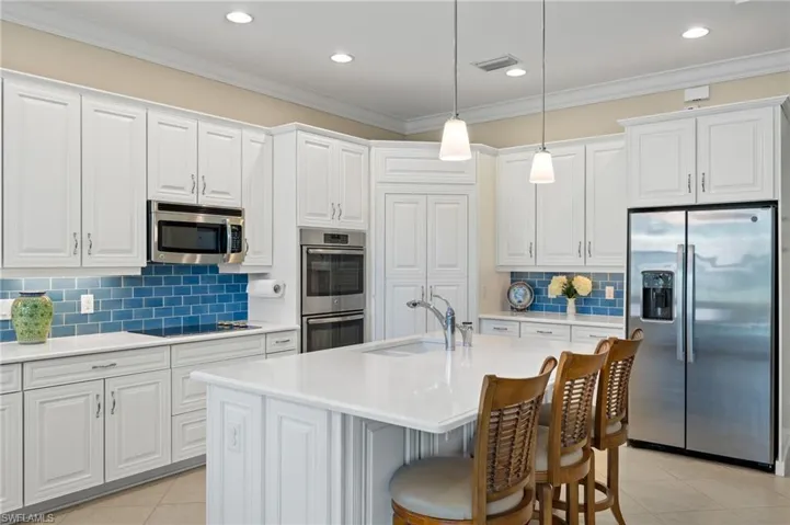 Kitchen featuring stainless steel appliances, sink, decorative light fixtures, a center island with sink, and white cabinetry