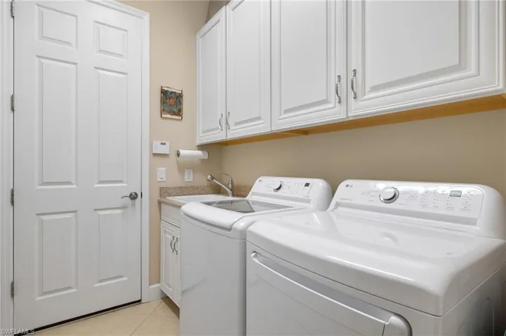 Laundry room with sink, light tile patterned flooring, cabinets, and independent washer and dryer