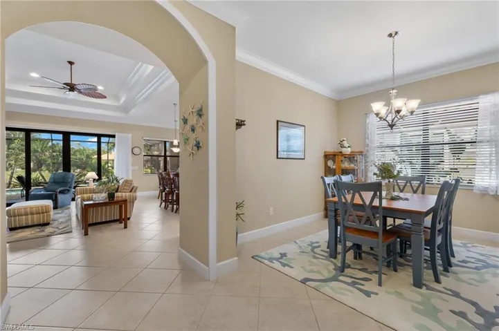 Dining space with ceiling fan with notable chandelier, a raised ceiling, ornamental molding, and light tile patterned flooring