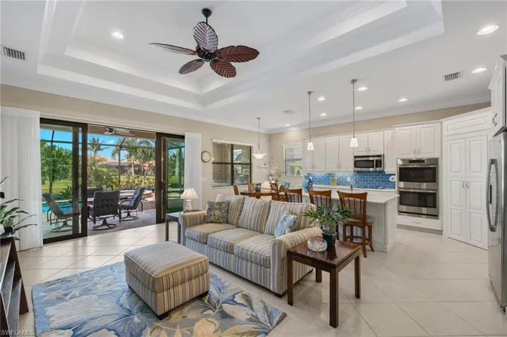 Living room with ceiling fan, crown molding, light tile patterned floors, and a tray ceiling