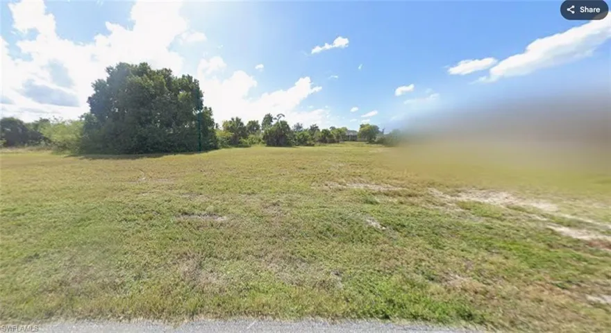 Expansive lot featuring a large grassy area, scattered mature trees, and a clear sky with clouds
