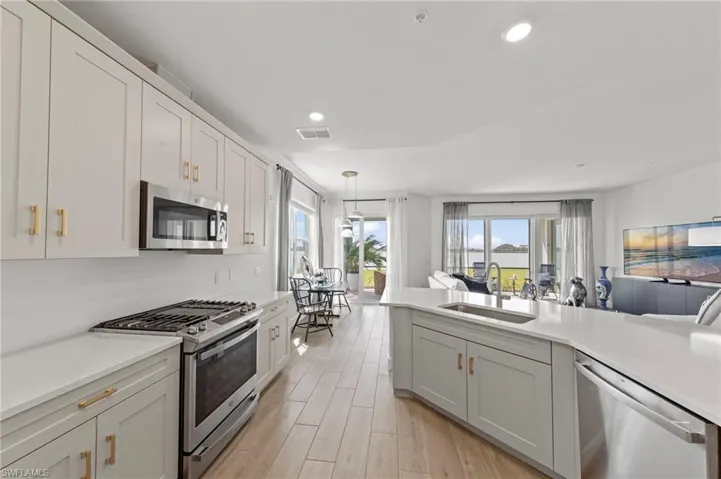 Kitchen featuring stainless steel appliances, light wood-style floors, open floor plan, and light stone counters