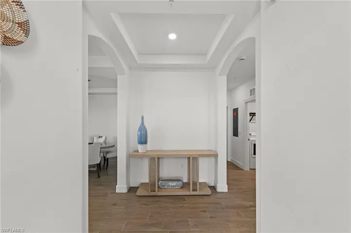 Hallway with arched walkways, wood finished floors, a tray ceiling, and recessed lighting