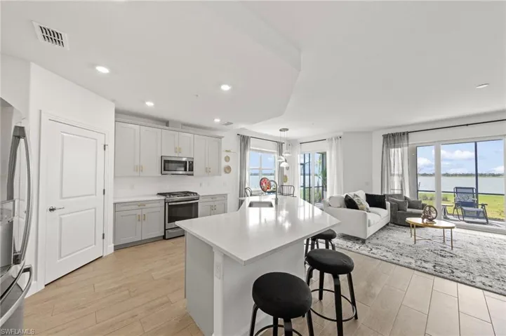 Kitchen with stainless steel appliances, a kitchen bar, a center island with sink, open floor plan, and light wood-type flooring