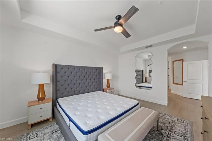 Bedroom with a raised ceiling, light wood finished floors, arched walkways, ceiling fan, and recessed lighting