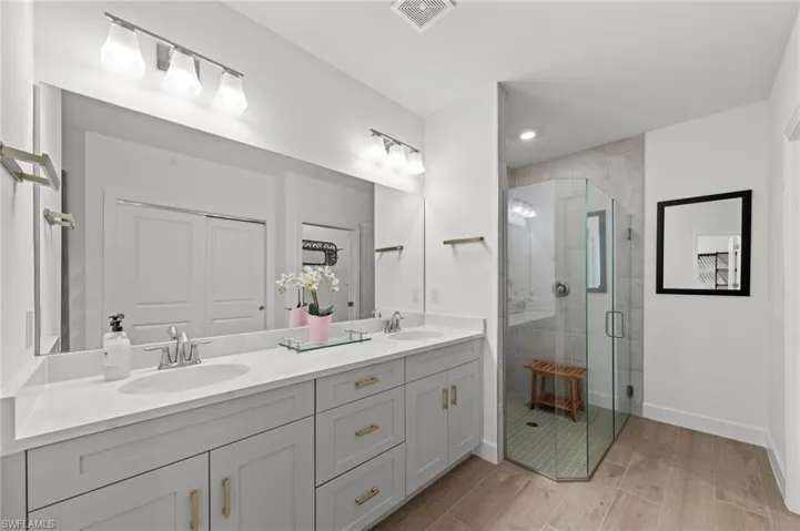 Full bath with a shower stall, double vanity, wood finish floors, and a closet
