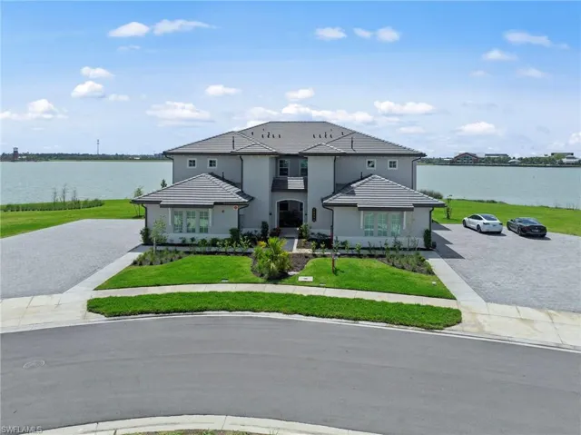 View of front facade with a water view, a front lawn, stucco siding, and decorative driveway