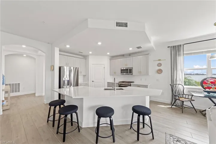 Kitchen with light wood-style floors, arched walkways, an island with sink, a kitchen breakfast bar, and light stone counters