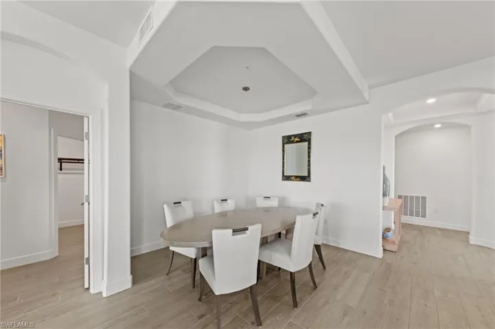 Dining area with arched walkways, light wood-type flooring, and a tray ceiling