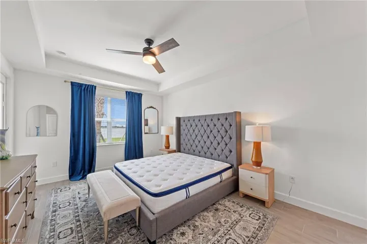 Bedroom with a tray ceiling, light wood-type flooring, and ceiling fan