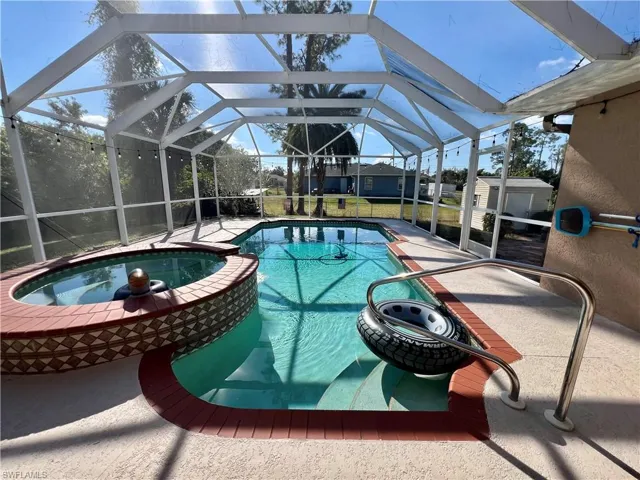 View of pool featuring screen enclosure, an in ground hot tub, and a spacious patio