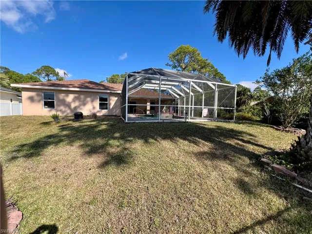 Back of property with screen enclosure, a yard, and a patio