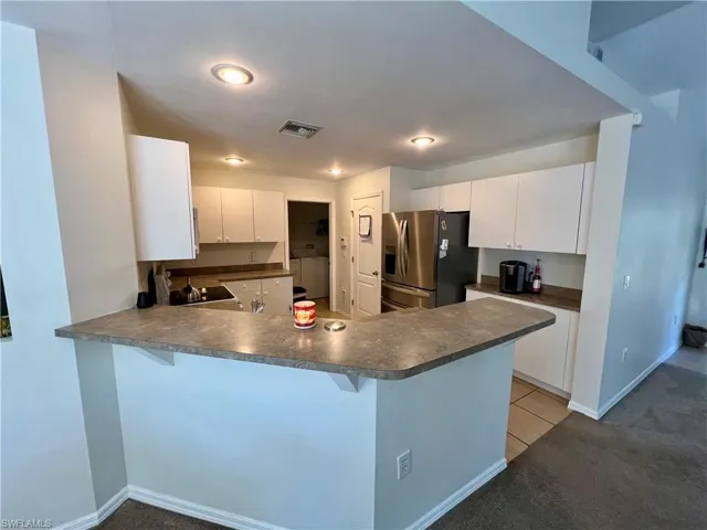 Kitchen with white cabinetry, stainless steel French door fridge with ice dispenser, kitchen peninsula