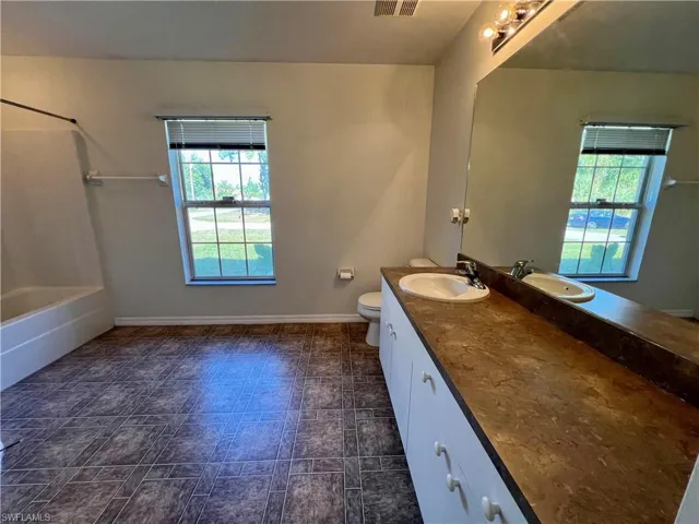 Full bathroom featuring vanity, a healthy amount of sunlight, toilet, and bathtub / shower combination