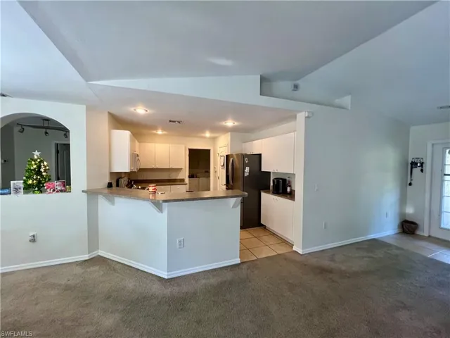 Kitchen featuring kitchen peninsula, vaulted ceiling, stainless steel fridge,  and white cabinetry