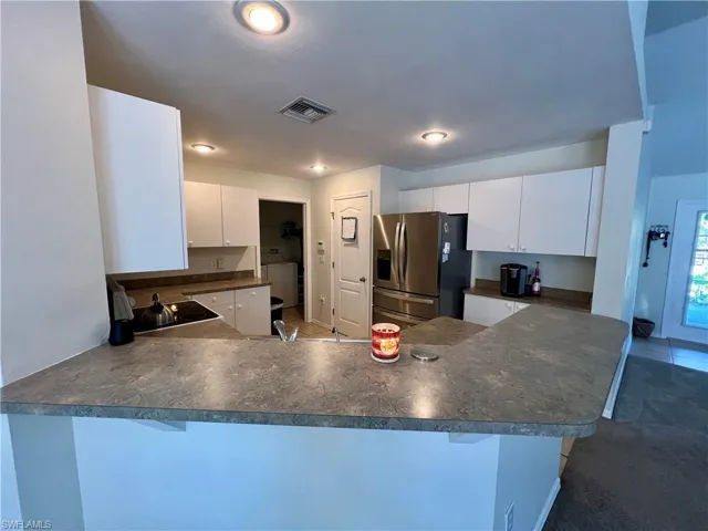Kitchen featuring kitchen peninsula, stainless steel fridge, sink, white cabinetry, and a breakfast bar area