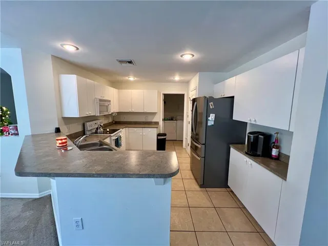 Kitchen featuring white cabinetry, peninsula, appliances, and light tile patterned flooring
