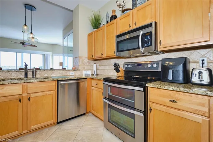 Kitchen featuring stainless steel appliances, hanging light fixtures, a ceiling fan, and light stone countertops
