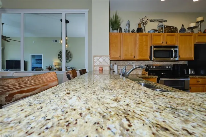 Kitchen with electric stove, light stone counters, stainless steel microwave, and wood finish cabinets