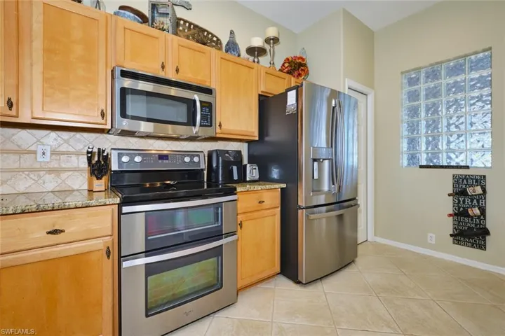 Kitchen featuring stainless steel appliances, light stone counters, light tile patterned floors, and tasteful backsplash