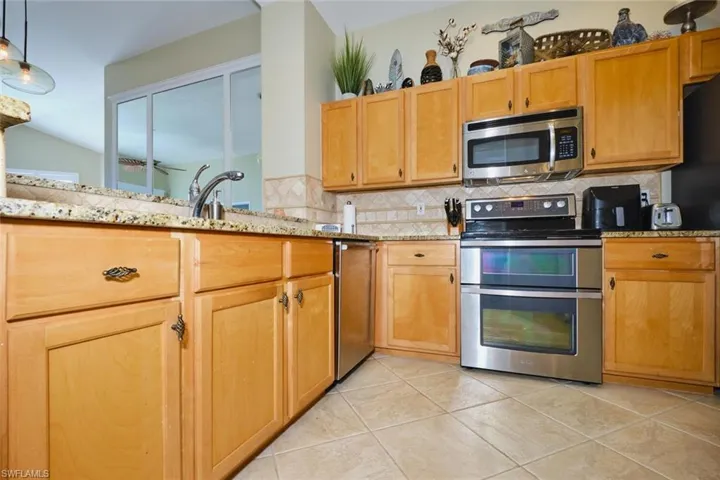 Kitchen with stainless steel appliances, light tile patterned floors, light stone countertops, tasteful backsplash, and decorative light fixtures
