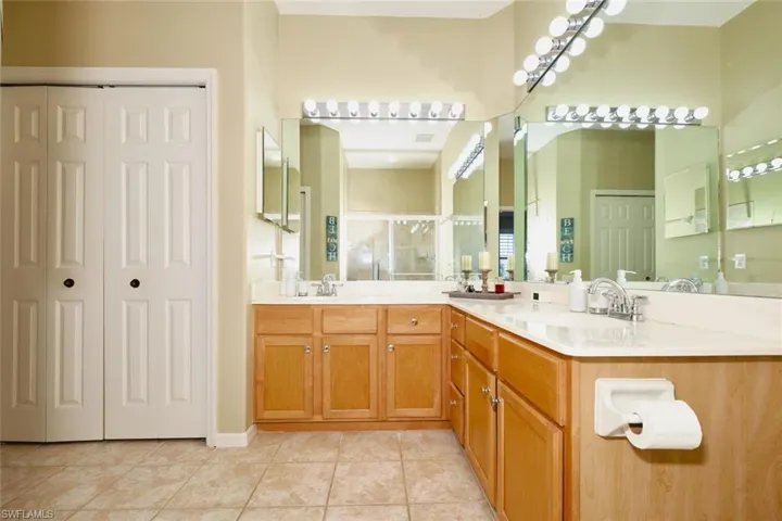 Bathroom featuring double vanity, a stall shower, a closet, and light tile patterned floors