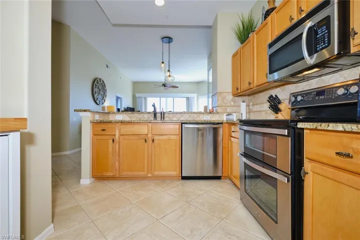 Kitchen featuring stainless steel appliances, light tile patterned flooring, hanging light fixtures, a peninsula, and backsplash