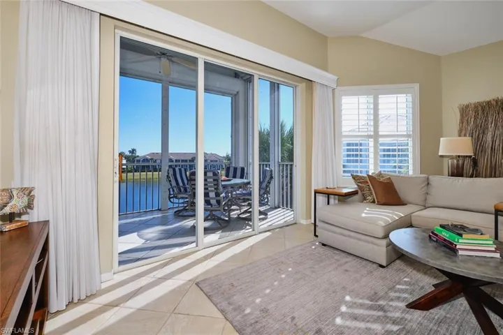 Living room with a water view, light tile patterned floors, vaulted ceiling, and a ceiling fan