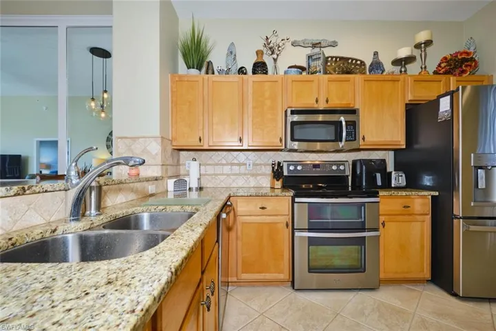 Kitchen featuring stainless steel appliances, light stone counters, decorative light fixtures, and backsplash