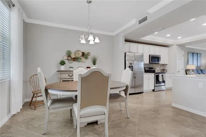 Dining room with ornamental molding, hanging lights, a tray ceiling, and light tile patterned floors