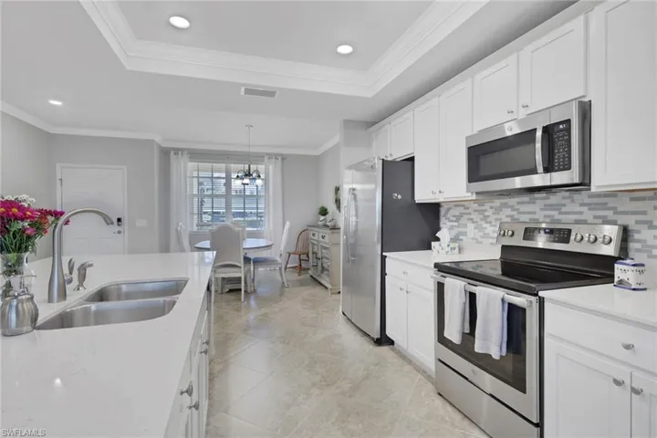 Kitchen featuring stainless steel appliances, white cabinetry, a raised ceiling, backsplash, and light stone countertops