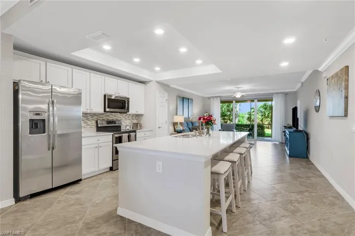 Kitchen featuring stainless steel appliances, white cabinets, a breakfast bar, a center island with sink, and recessed lighting